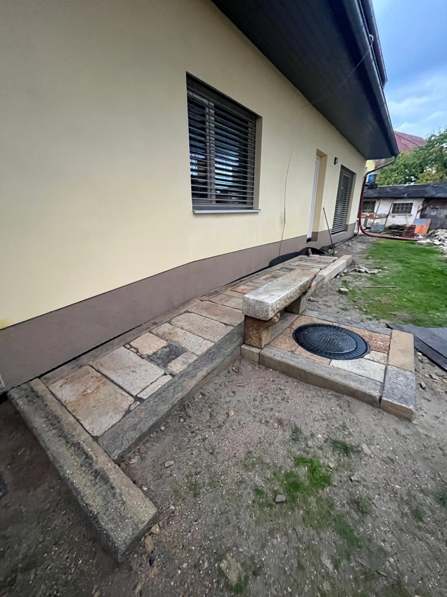 Venkovní dlažba z přírodního kamene podél domu s kamennou lavičkou